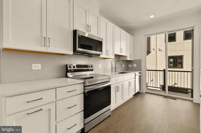 a kitchen with stainless steel appliances granite countertop white cabinets a sink a stove a microwave and a refrigerator