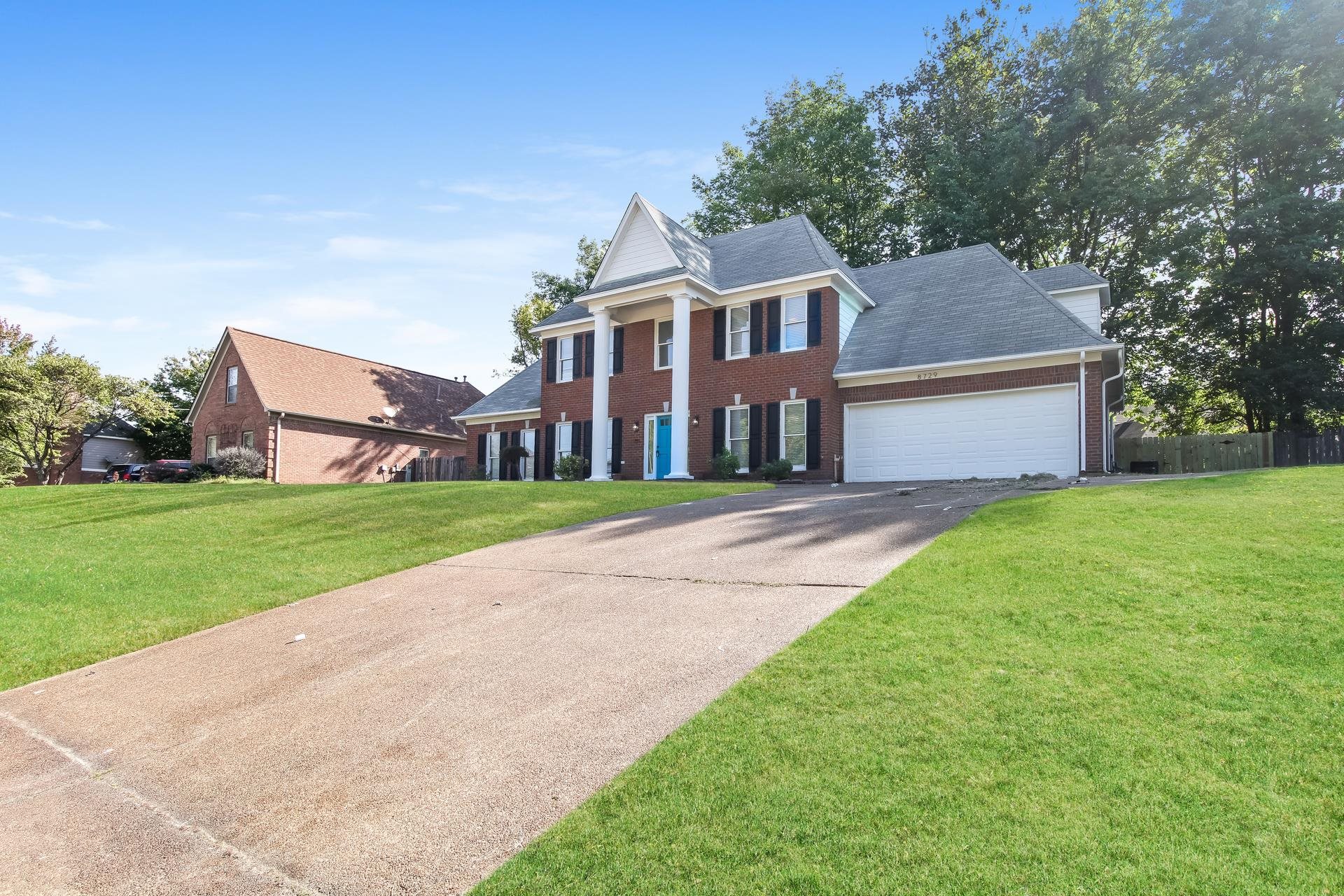 Greek revival house featuring brick siding, an attached garage, a front yard, and driveway