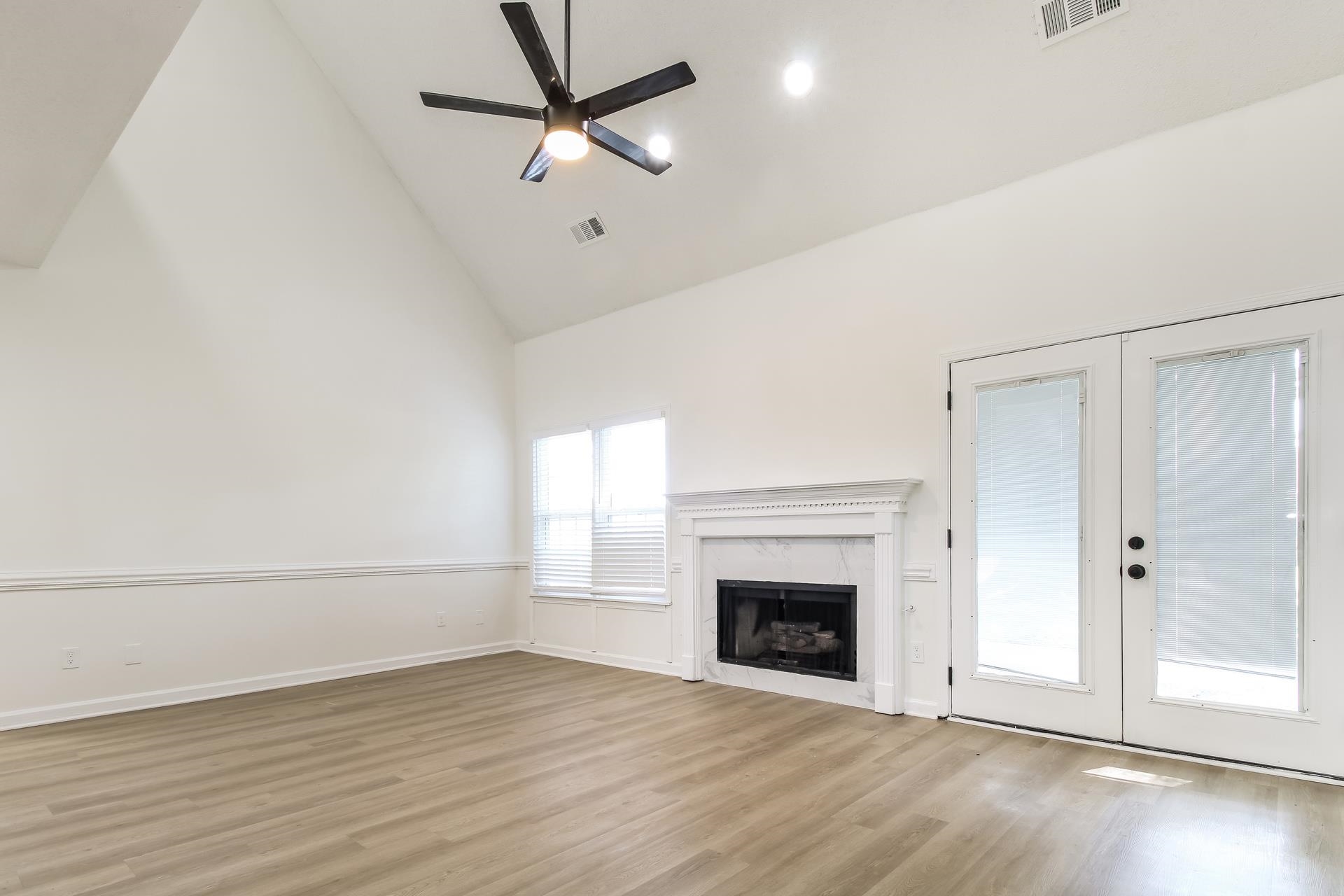Unfurnished living room featuring high vaulted ceiling, light wood-style floors, a high end fireplace, a ceiling fan, and french doors