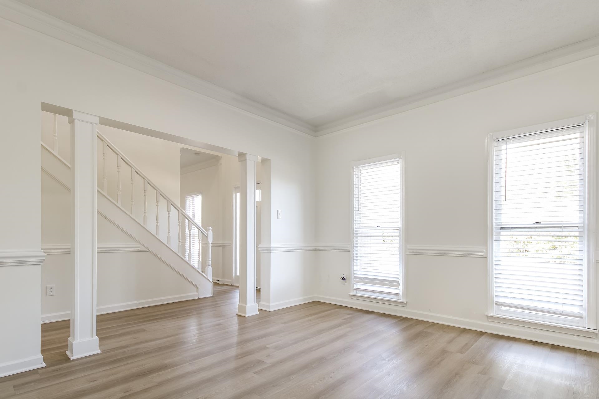 Empty room with stairs, crown molding, light wood-style flooring, and ornate columns