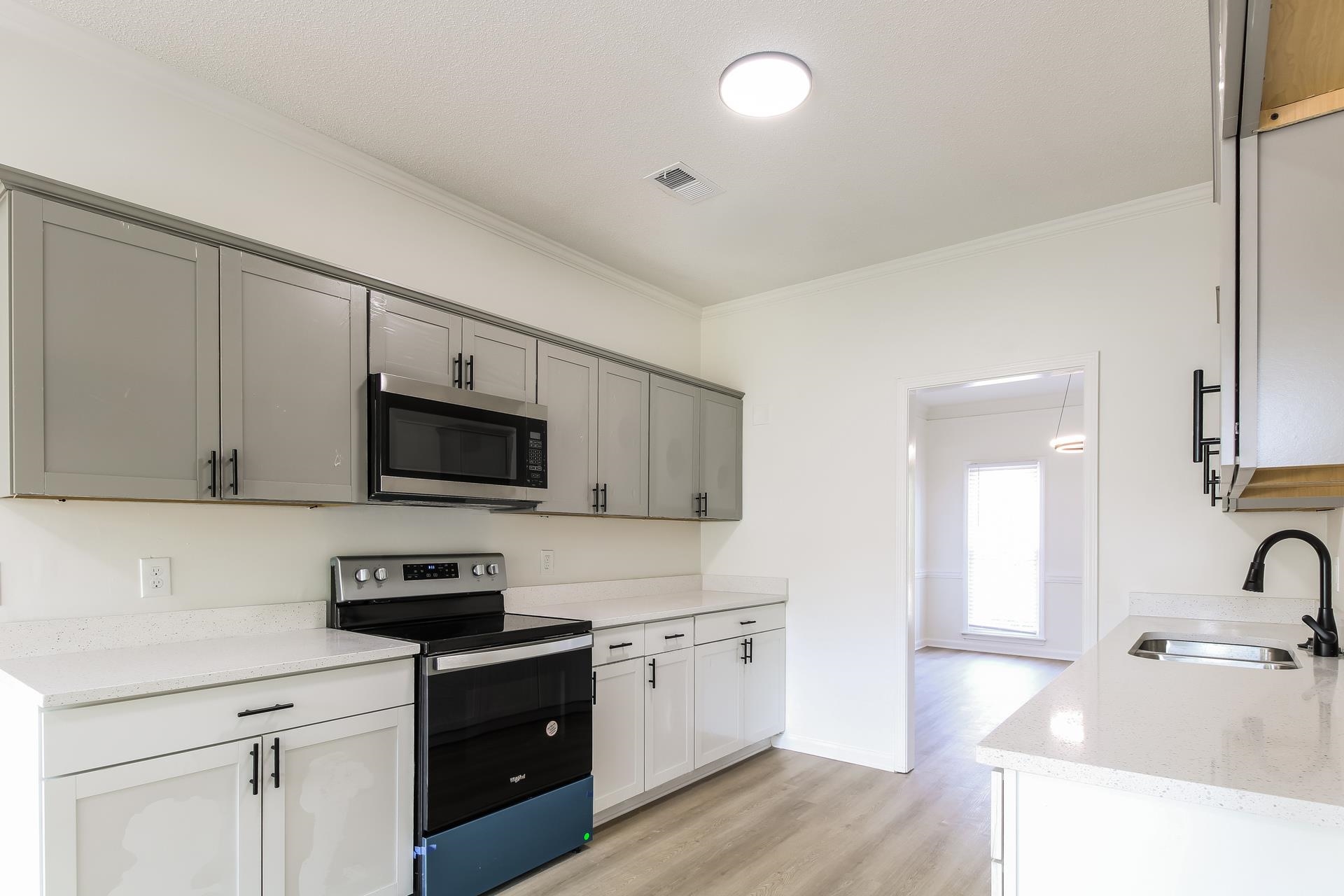 Kitchen featuring stainless steel appliances, ornamental molding, light wood-style floors, and light stone countertops