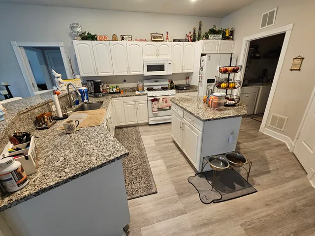 a kitchen with granite countertop a sink dishwasher stove and white cabinets with wooden floor