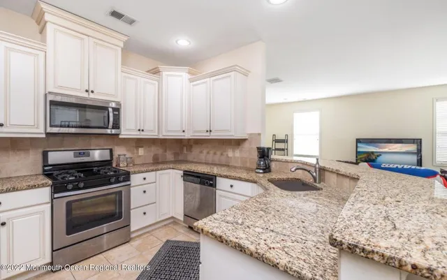 a kitchen with granite countertop a sink a stove top oven and cabinetry