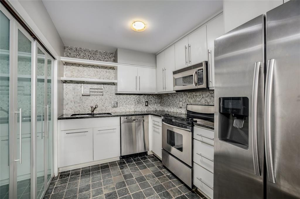 a kitchen with stainless steel appliances granite countertop a stove a sink and a refrigerator with white cabinets
