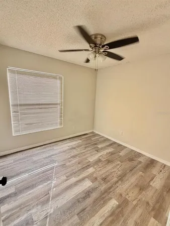 an empty room with wooden floor fan and windows
