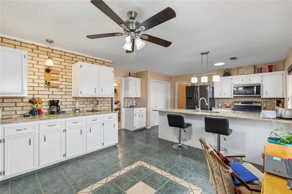 a kitchen with stainless steel appliances kitchen island granite countertop a refrigerator a stove a sink and white cabinets with wooden floor