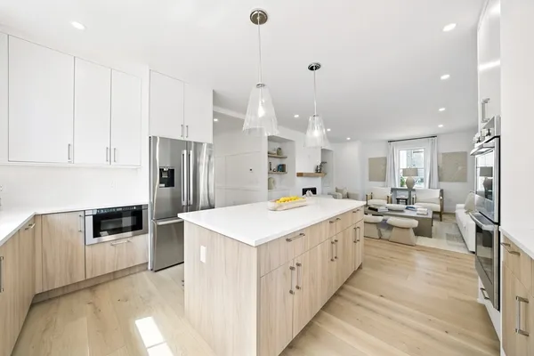 a large kitchen with kitchen island a stove a sink a refrigerator and white cabinets with wooden floor