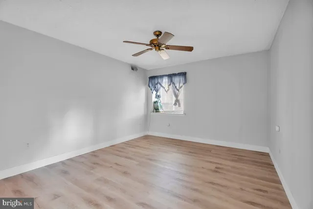 an empty room with wooden floor chandelier fan and windows