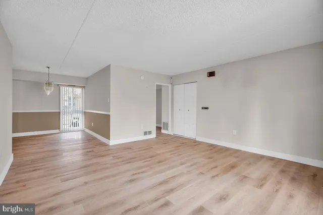 a view of an empty room with wooden floor and a kitchen