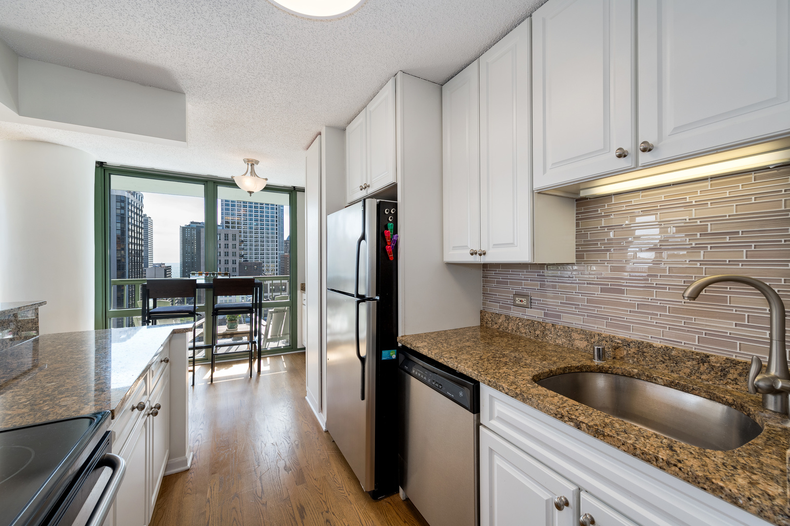 111 West Maple Street, Unit 1601 Chicago, IL 60610 - Photo 12 of 24 a kitchen with granite countertop a refrigerator a sink a stove and white cabinets with wooden floor