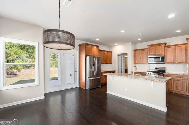 a kitchen with stainless steel appliances kitchen island granite countertop a refrigerator a stove a microwave oven a sink with island and chairs with wooden floor