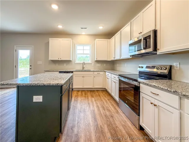 a kitchen with granite countertop a stove a sink and white cabinets with wooden floor