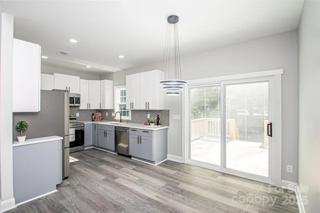 a open kitchen with stainless steel appliances granite countertop a refrigerator a sink dishwasher a oven with white cabinets and wooden floor