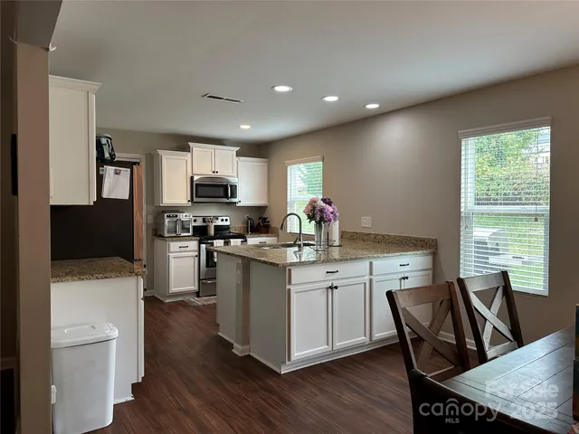 a kitchen with stainless steel appliances granite countertop a stove a sink a microwave a refrigerator white cabinets and wooden floor