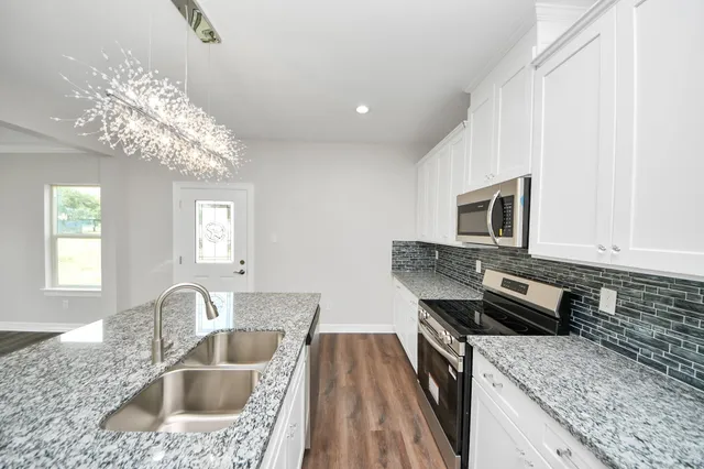 a kitchen with granite countertop a sink dishwasher stove and microwave with wooden floor