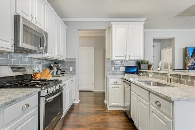 a kitchen with stainless steel appliances granite countertop a stove top oven a sink dishwasher and white cabinets with wooden floor