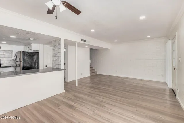 a view of an empty room with wooden floor and a ceiling fan
