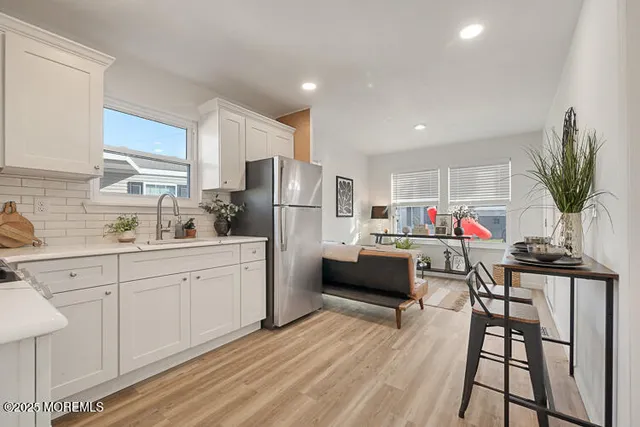 a kitchen with stainless steel appliances a refrigerator a sink dishwasher a dining table and chairs with wooden floor