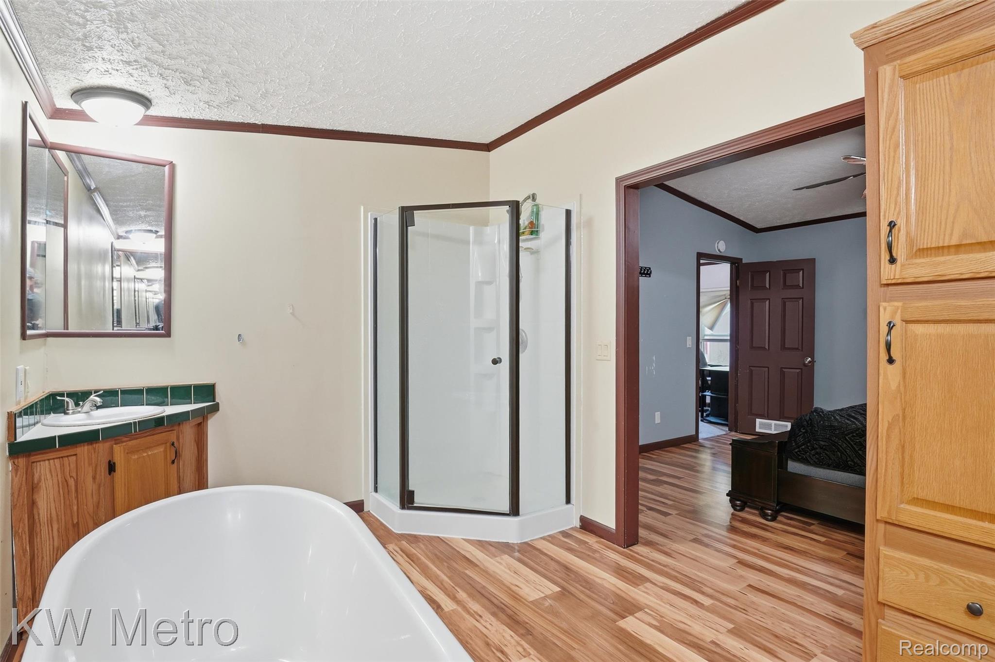 22733 Sumpter Road Belleville, MI 48111 - Photo 14 of 52 Freestanding bathtub with corner glass-enclosed shower, wood-finish flooring, wood cabinetry with green tile countertop, and a medicine cabinet with mirror