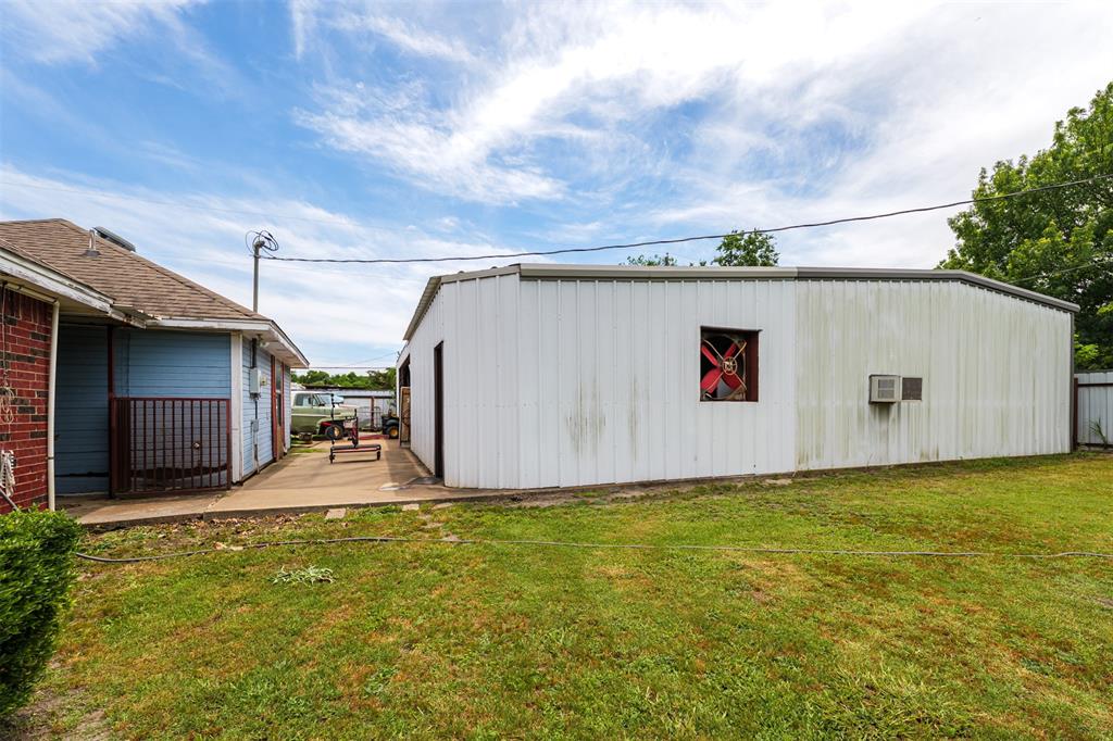 601 Houston School Road Red Oak, TX 75154 - Photo 14 of 32 Expansive grass lawn with a concrete walkway, featuring a metal-sided outbuilding with an exterior fan and an additional structure with brick and blue siding