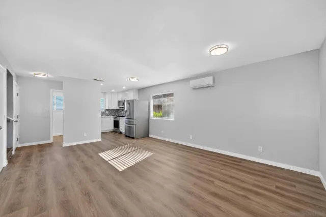 a view of an empty room with wooden floor and a kitchen