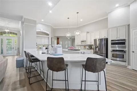 a kitchen with granite countertop a refrigerator oven a sink dishwasher and white cabinets with wooden floor