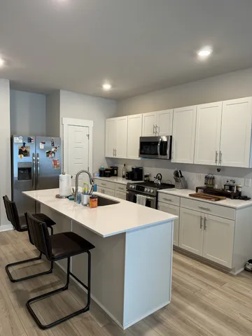 a kitchen with stainless steel appliances a table chairs sink refrigerator and cabinets