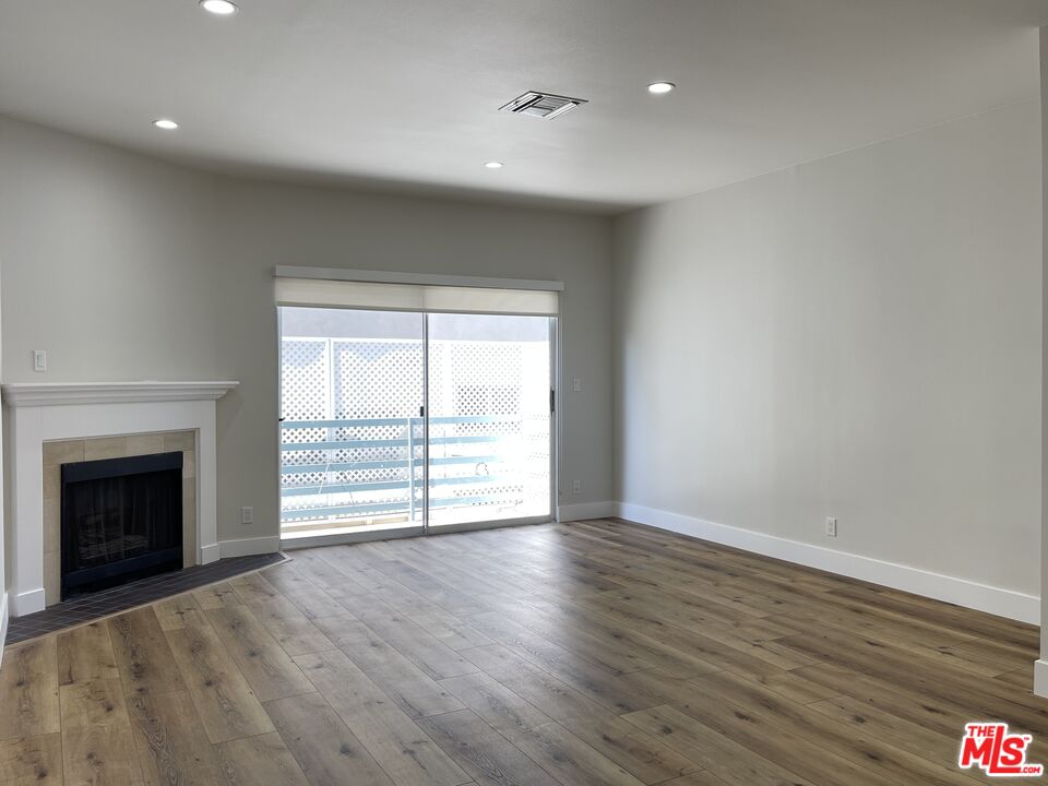 11738 Mayfield Avenue, Unit 114 Los Angeles, CA 90049 - Photo 9 of 25 an empty room with wooden floor fireplace and windows