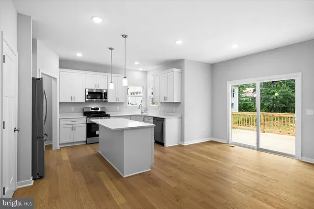 a kitchen with stainless steel appliances granite countertop a refrigerator a sink dishwasher a stove and white countertops with wooden floor