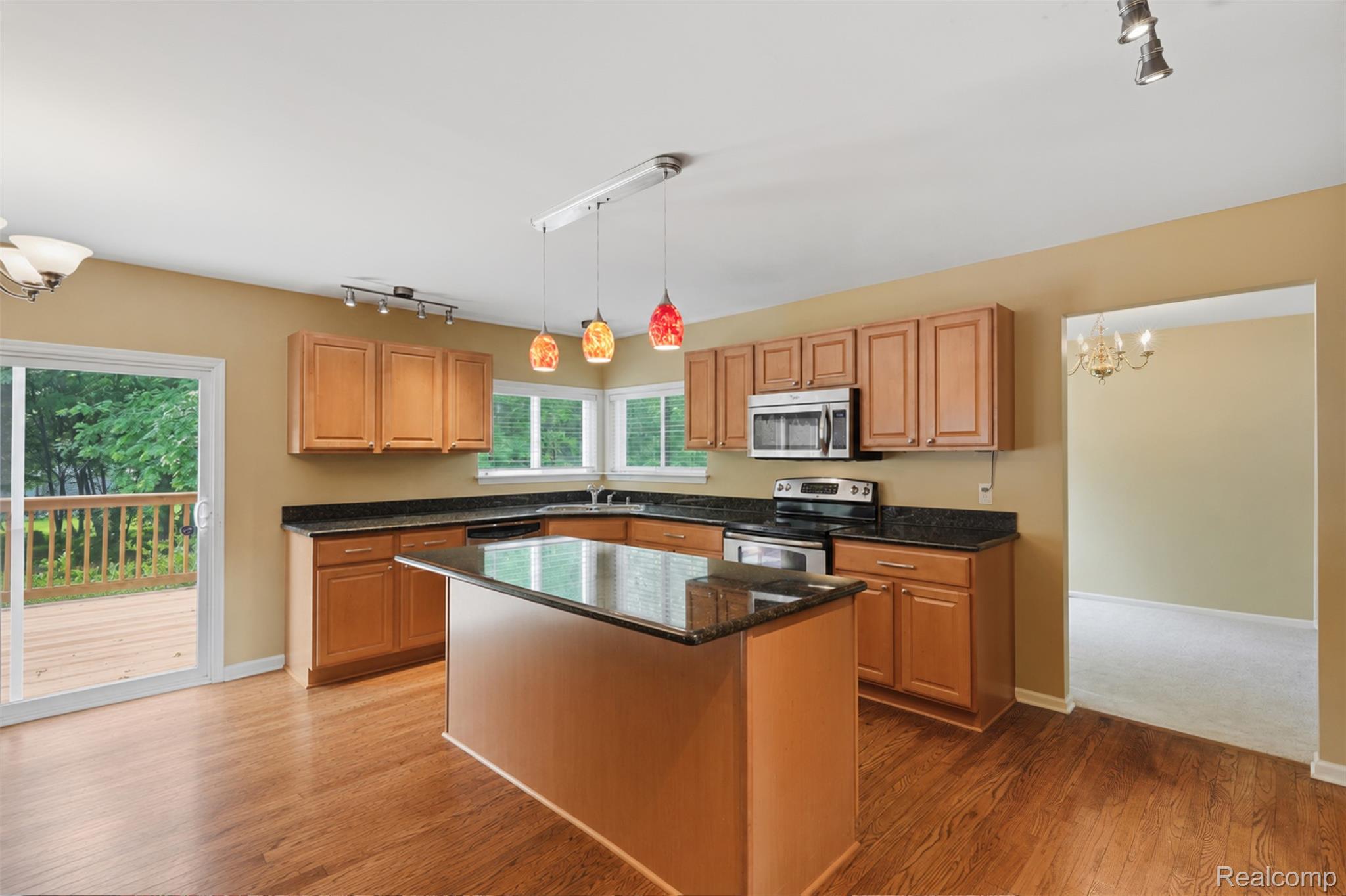 170 Fairhill Way Howell, MI 48843 - Photo 21 of 46 Kitchen featuring wood-finish flooring, an island with dark stone countertop, wood cabinetry, stainless steel appliances, and a sliding glass door opening to an exterior deck