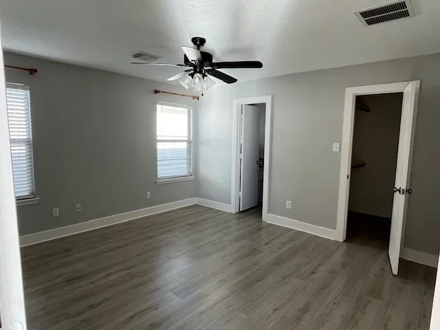 an empty room with wooden floor fan and windows