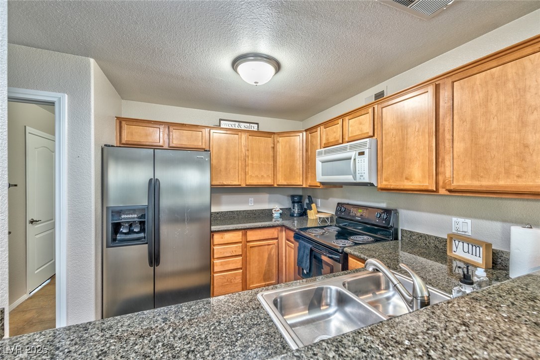 3145 East Flamingo Road, Unit 2068 Las Vegas, NV 89121 - Photo 6 of 15 Kitchen featuring stainless steel fridge with ice dispenser, electric range, white microwave, a textured ceiling, and brown cabinets