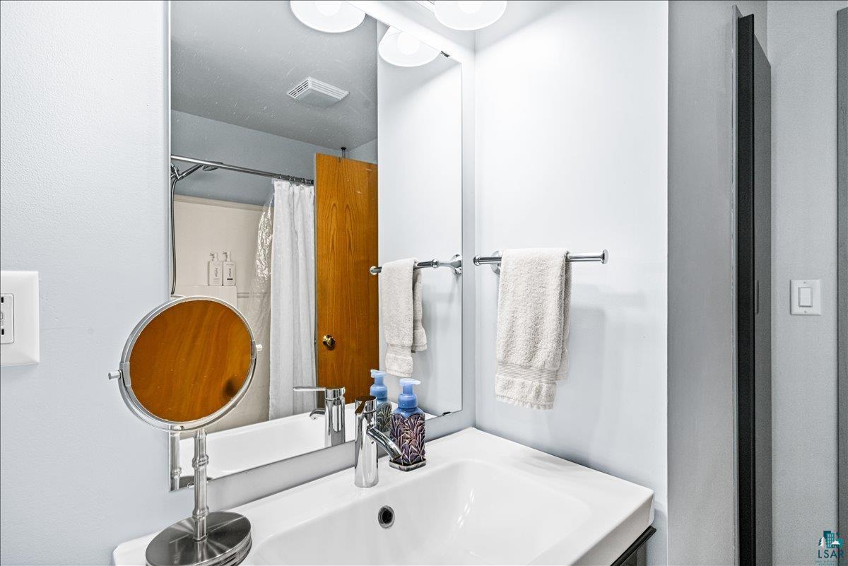 130 West Austin Street Duluth, MN 55803 - Photo 15 of 35 Bathroom featuring a rectangular vanity mirror, a white ceramic sink with a chrome faucet, overhead vanity lighting, and a towel bar