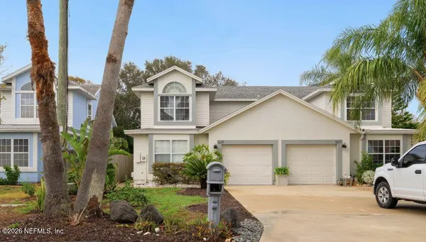 a view of a white house with a large windows and a yard with palm trees
