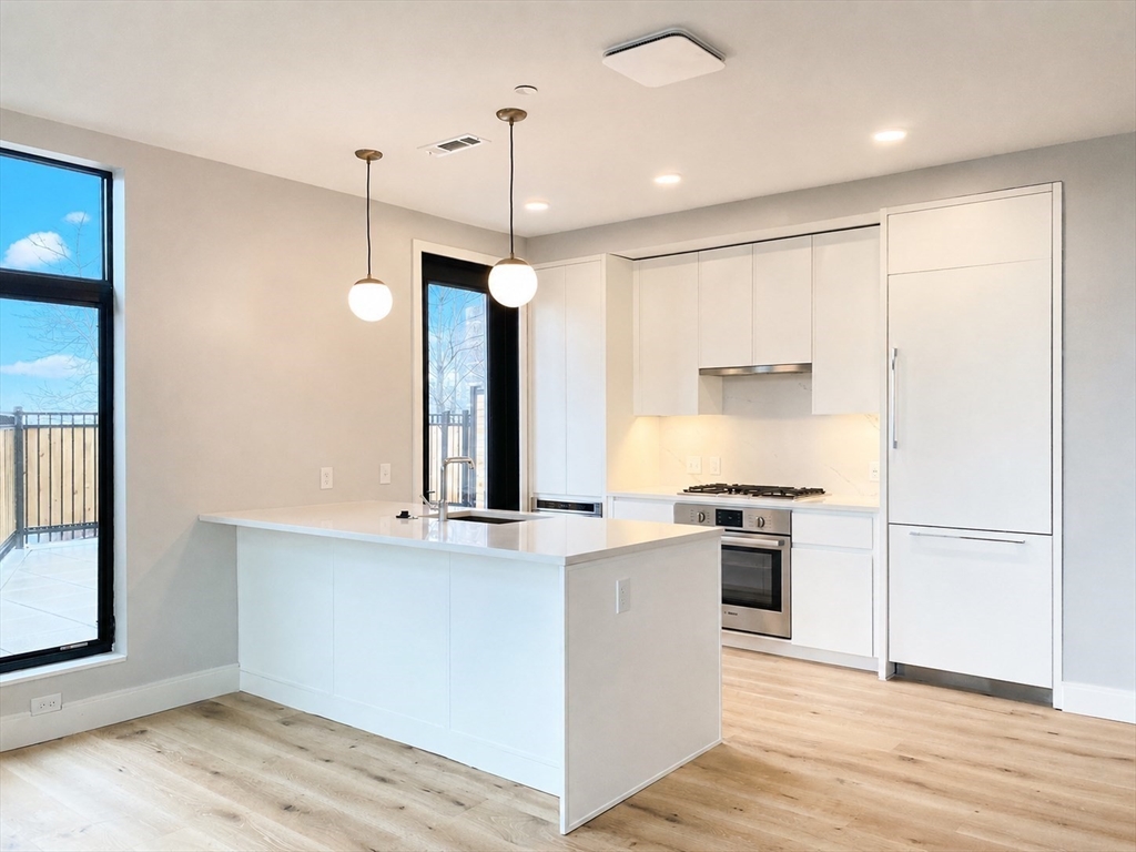 191 Washington Street, Unit 301 Boston, MA 02135 - Photo 5 of 40 a kitchen with stainless steel appliances granite countertop a stove a refrigerator and a sink with wooden floors