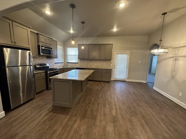 a kitchen with stainless steel appliances granite countertop a sink a stove a refrigerator and island with wooden floor