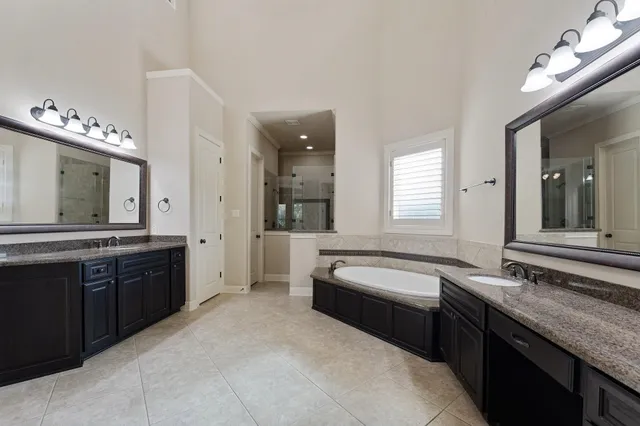 a spacious bathroom with a granite countertop double vanity sink a bathtub and mirror