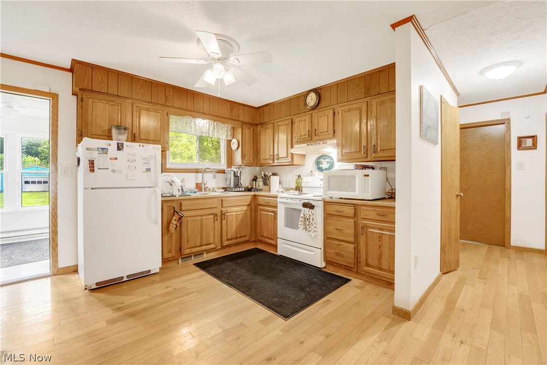 16107 Moseley Road Madison, OH 44057 - Photo 13 of 40 Kitchen featuring wood-finish flooring, wood cabinetry with paneling, white appliances, and a window above the sink