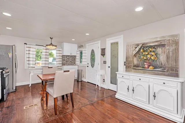 a kitchen with stainless steel appliances granite countertop a refrigerator a sink dishwasher a dining table and chairs with wooden floor