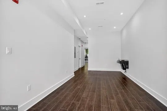 a view of a refrigerator in kitchen and an empty room with wooden floor