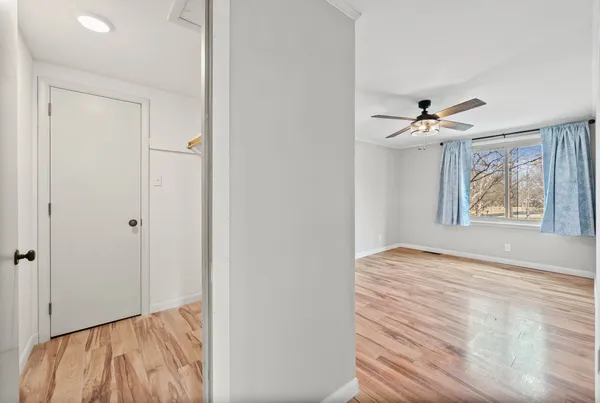 a view of an empty room with wooden floor and a ceiling fan