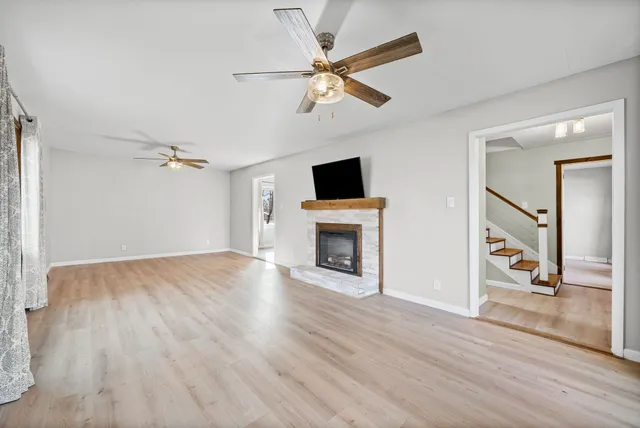 a view of a livingroom with a fireplace a ceiling fan and wooden floor