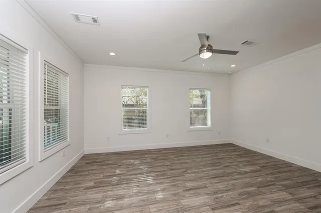 an empty room with wooden floor ceiling fan and windows