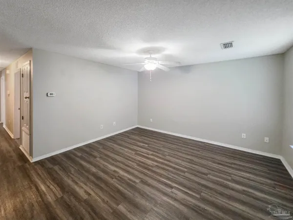 a view of an empty room with wooden floor and a ceiling fan