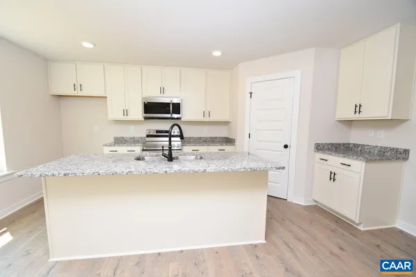 a kitchen with kitchen island granite countertop a sink a stove a refrigerator and white cabinets