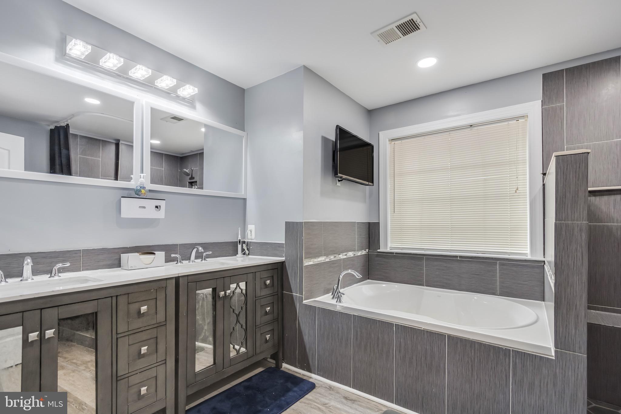 16607 Mannington Road Accokeek, MD 20607 - Photo 16 of 32 a bathroom with a tub a double vanity sink and a large mirror