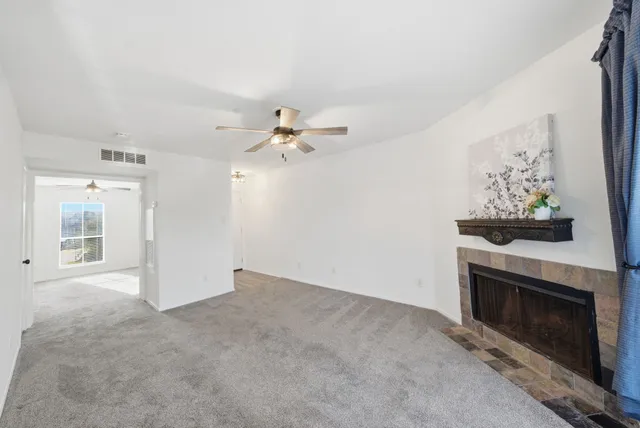 a view of an empty room with chandelier fan and fire place