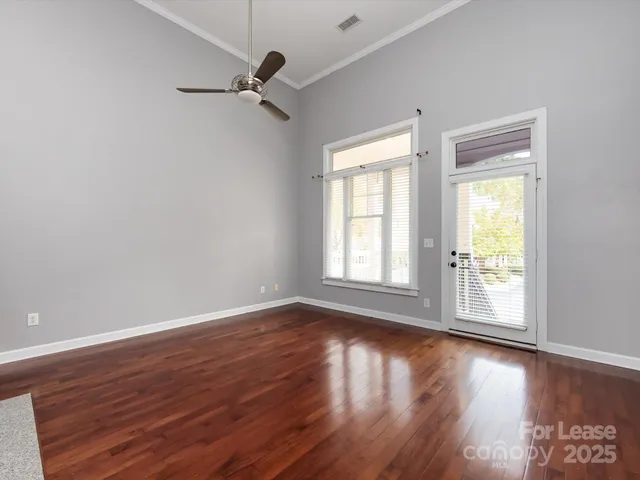 an empty room with wooden floor fan and windows