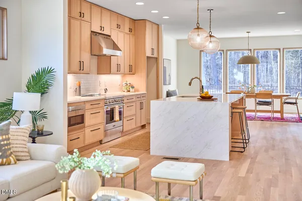 a kitchen with a stove a sink a kitchen island with chairs and wooden cabinets