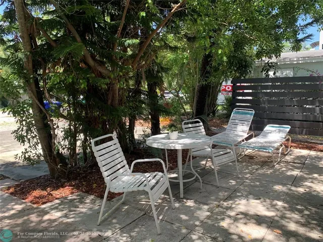 a view of a backyard with table and chairs potted plants and a large tree
